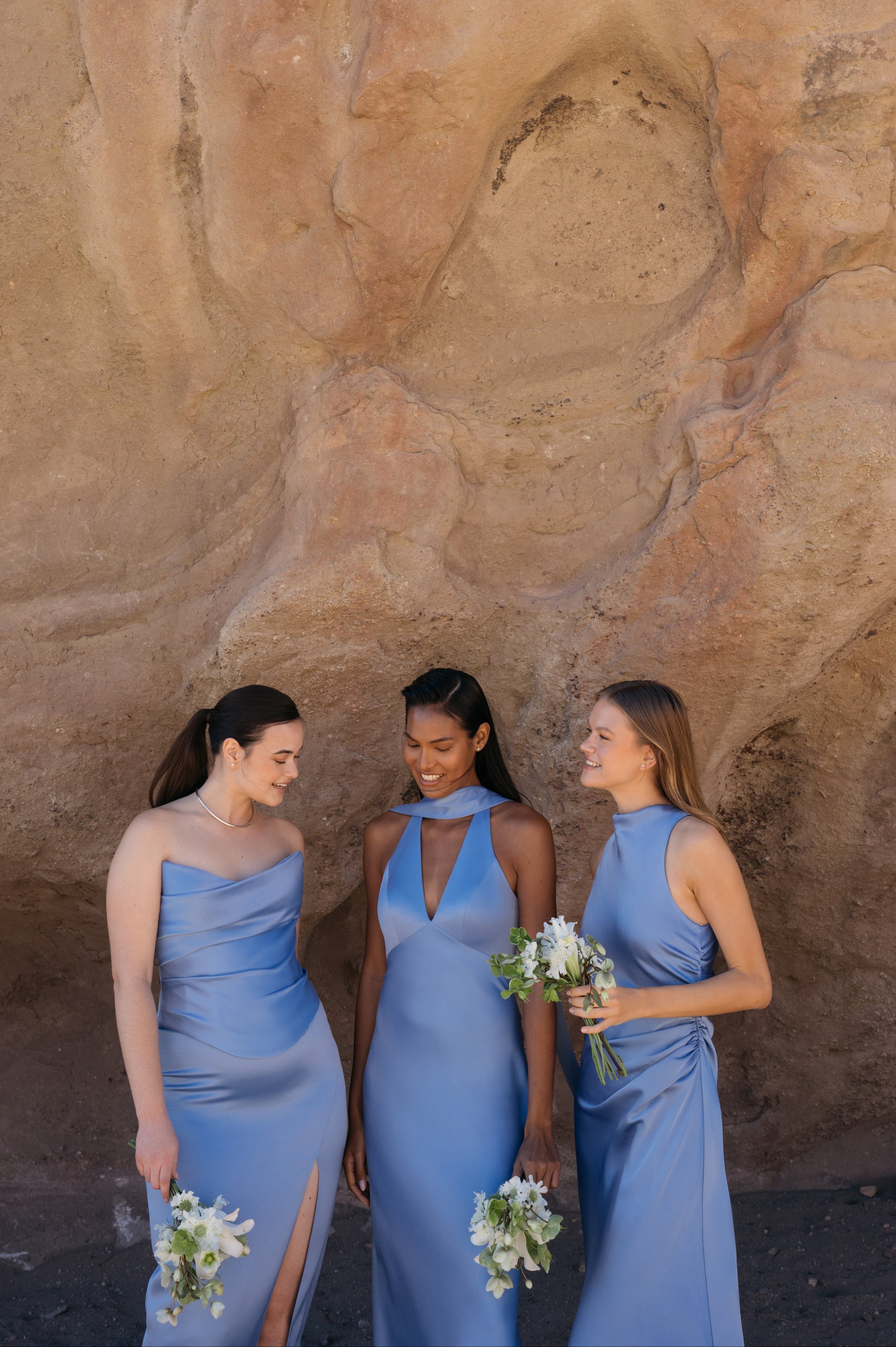 Three women in blue dresses standing against a rocky background